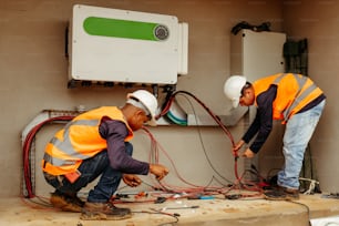 Deux hommes portant des casques de sécurité et des gilets de sécurité travaillent sur de l’équipement électrique