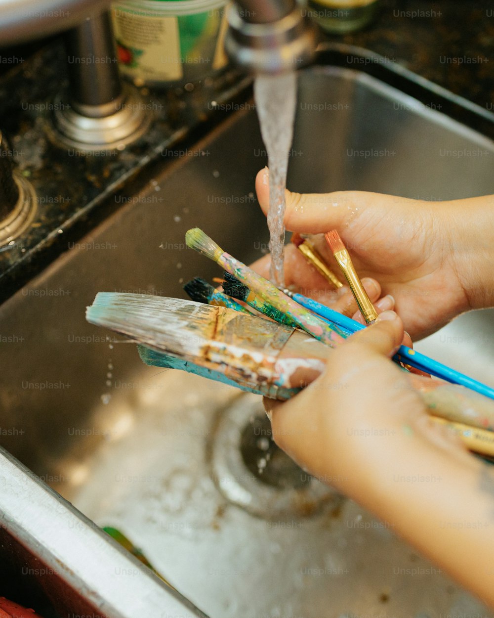uma pessoa lavando as mãos com escovas de dentes em uma pia