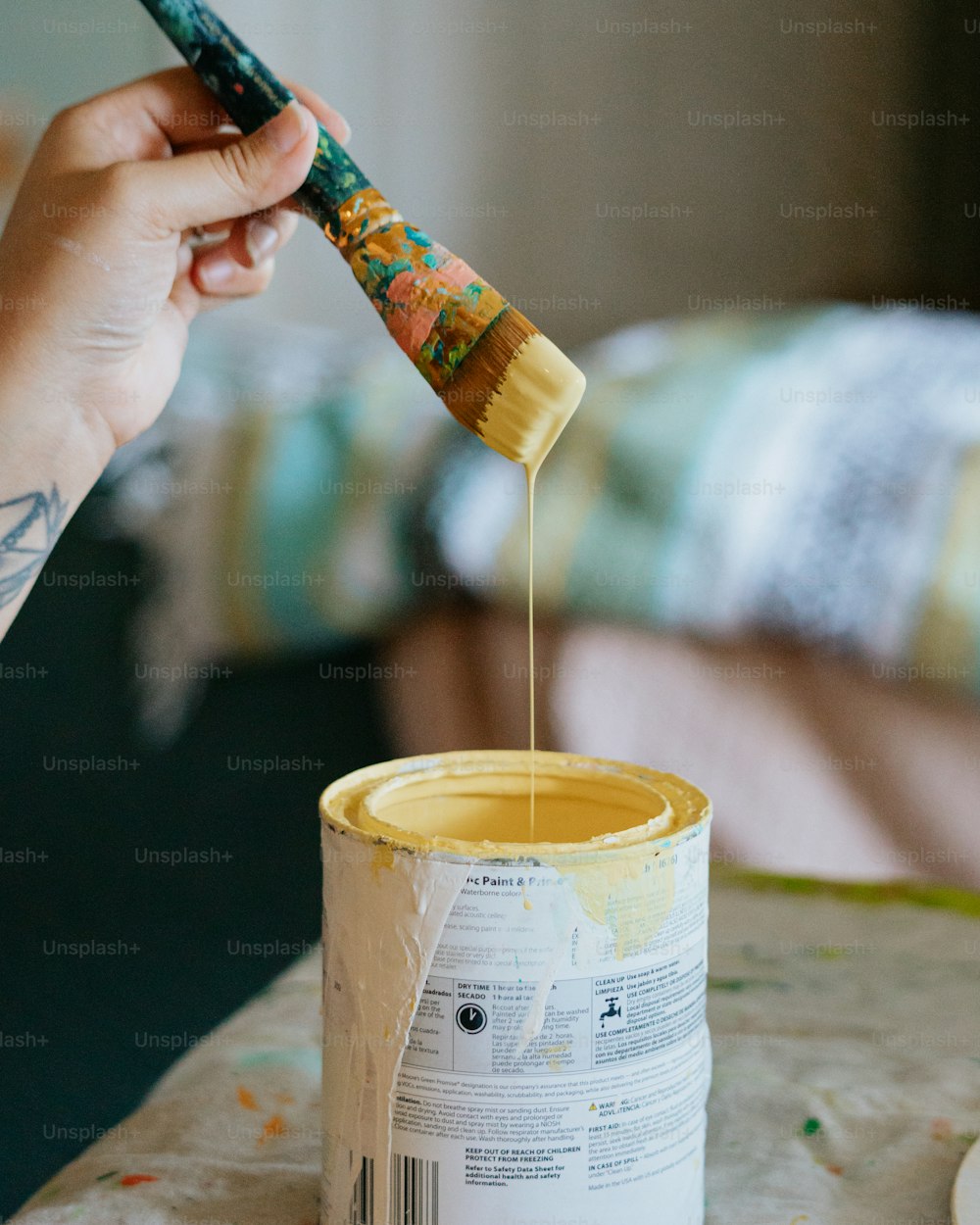 Una persona sosteniendo un pincel sobre una lata de pintura amarilla