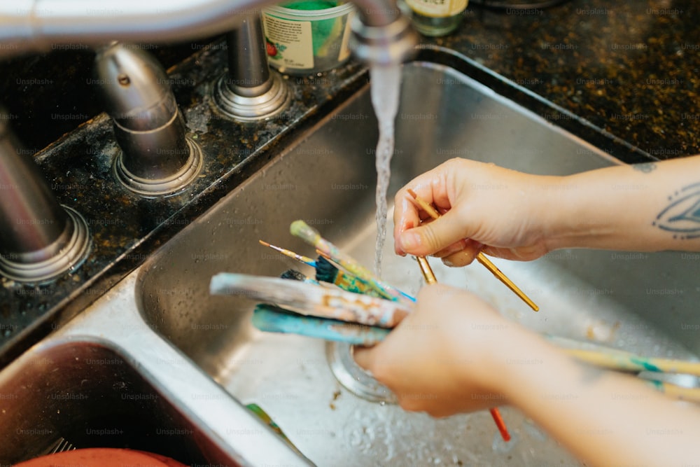 una persona che si lava le mani con spazzolini da denti in un lavandino