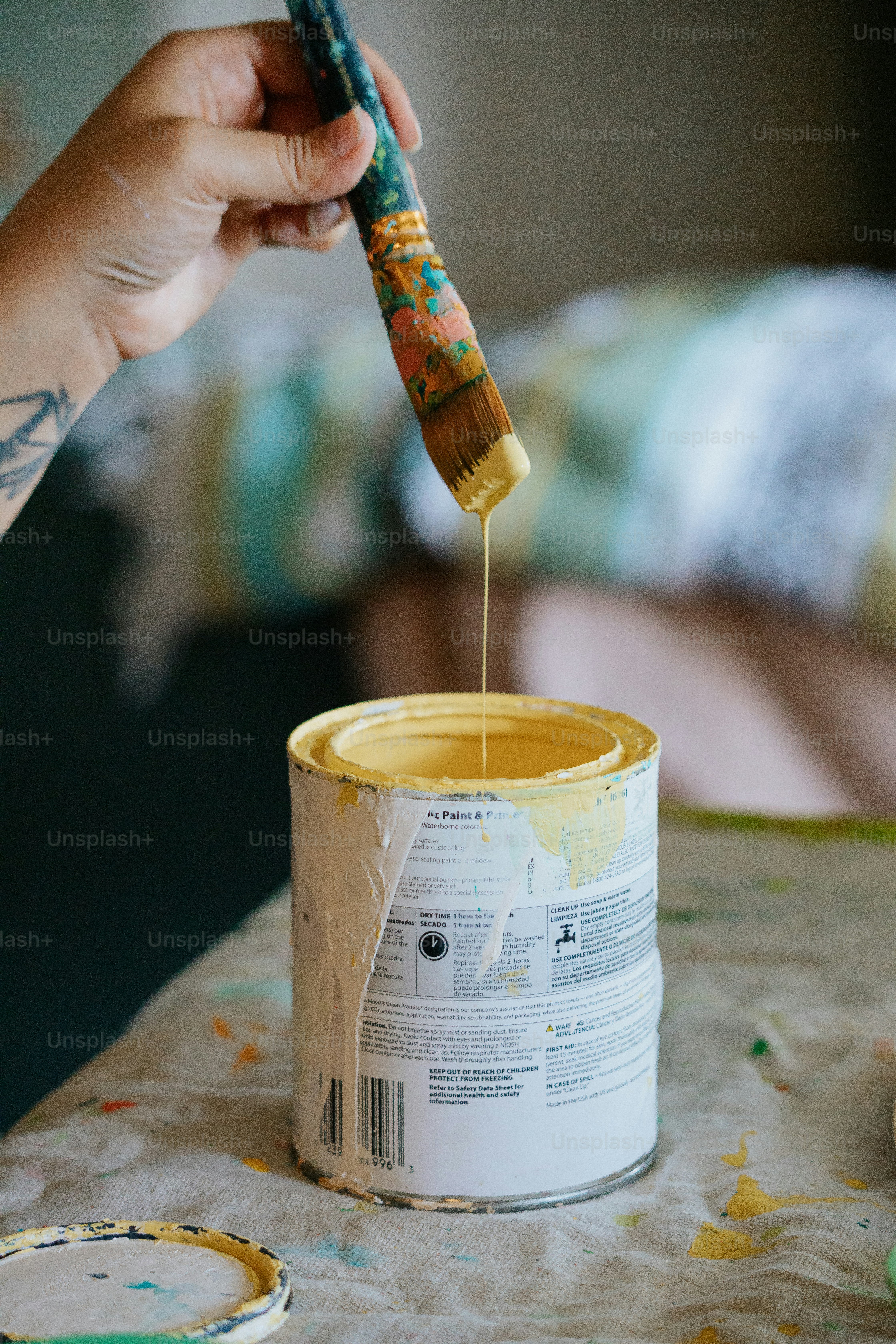 a person holding a paintbrush over a can of yellow paint