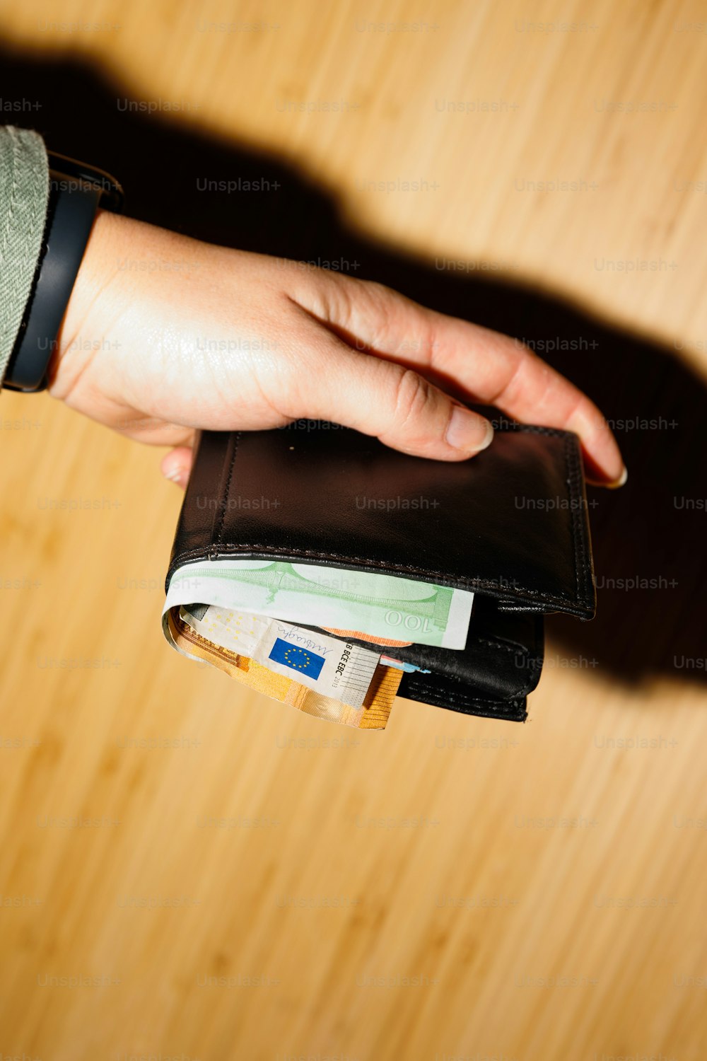 Die Hand einer Person, die eine Brieftasche auf einem Holztisch hält