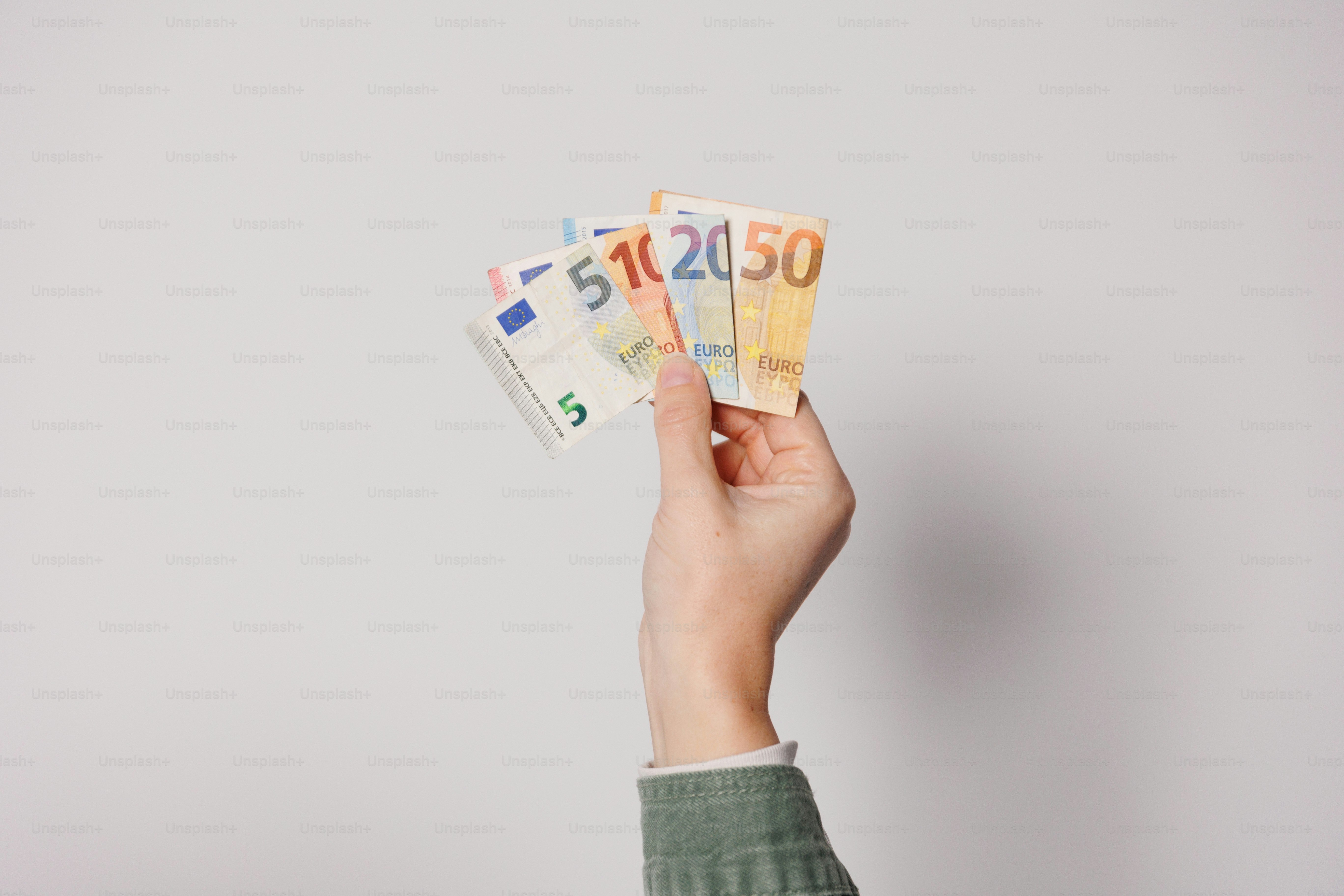 Die Hand einer Person, die fünf verschiedene Geldscheine hält