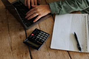 Una persona escribiendo en una computadora portátil junto a una calculadora