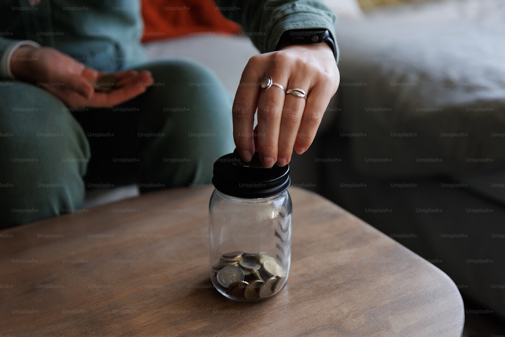 uma pessoa colocando moedas em um frasco em uma mesa