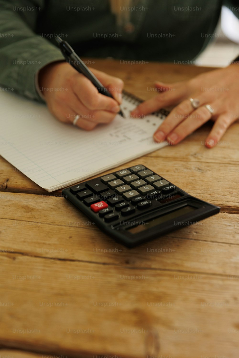 a person writing on a piece of paper next to a calculator