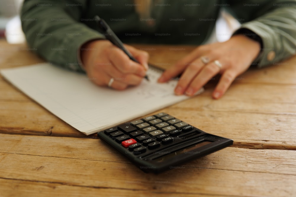 une personne écrivant sur un morceau de papier à côté d’une calculatrice