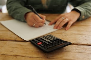 Una persona escribiendo en un pedazo de papel junto a una calculadora