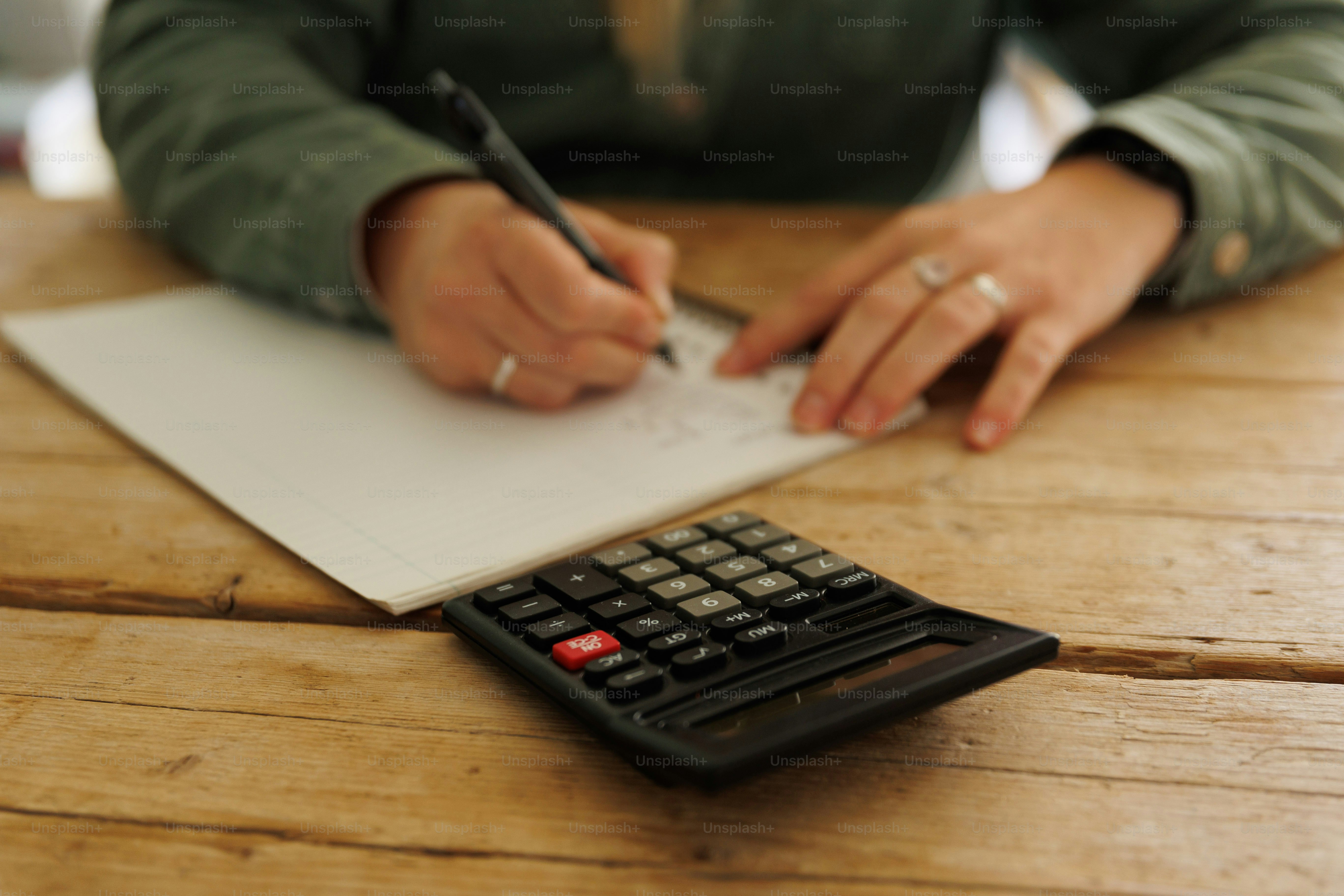 a person writing on a piece of paper next to a calculator