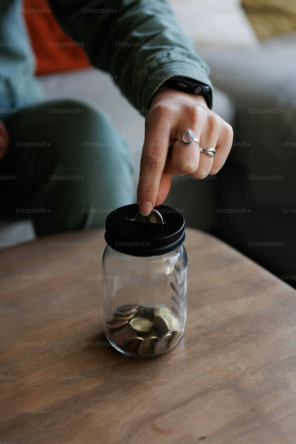 une personne mettant des pièces dans un bocal sur une table