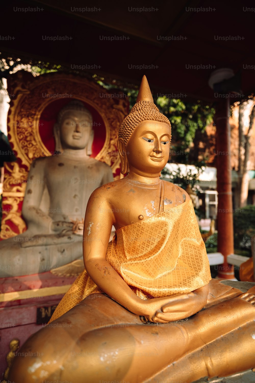 uma estátua dourada de buddha sentada no topo de uma estátua de madeira