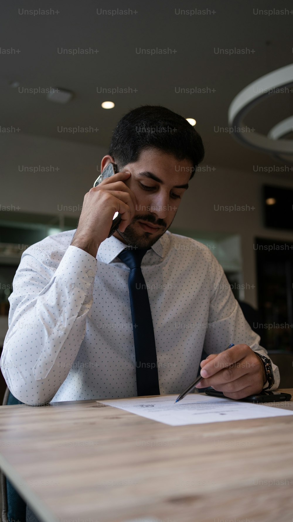 um homem sentado em uma mesa falando em um telefone celular