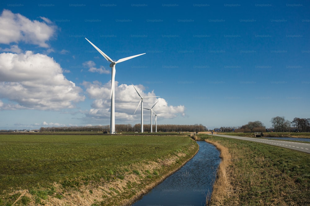 a river running through a lush green field next to wind turbines