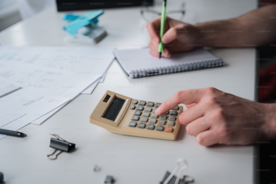 A person using a calculator on a desk with a notebook, representing the cost calculation work behind a custom plush production order