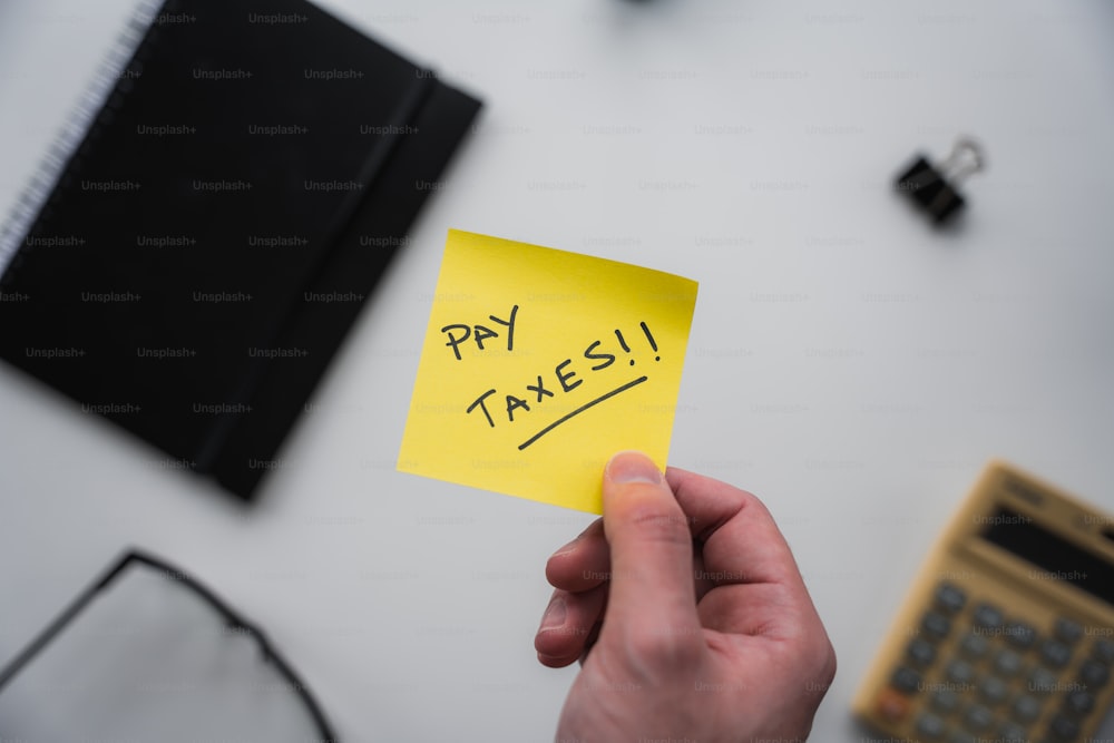 a person holding a sticky note with the words pay taxes written on it