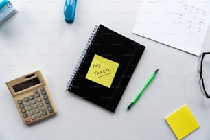 um bloco de notas, caneta, calculadora, óculos e uma calculadora