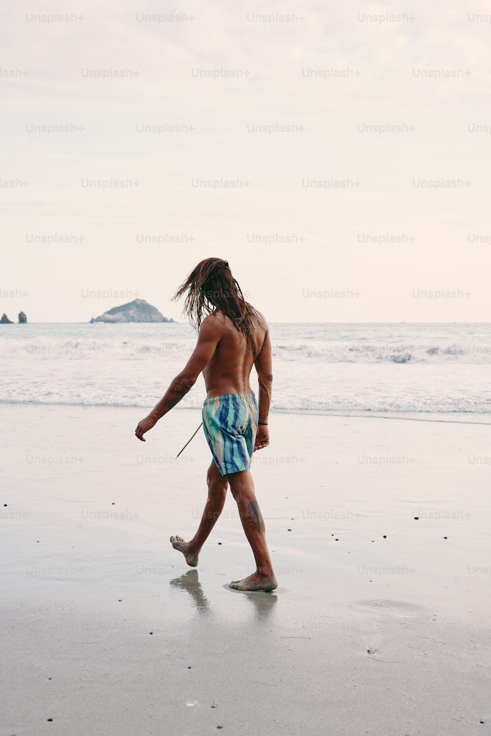 Un uomo con i dreadlocks che cammina sulla spiaggia