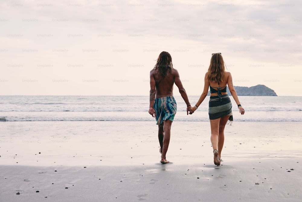 um homem e uma mulher que caminham na praia de mãos dadas