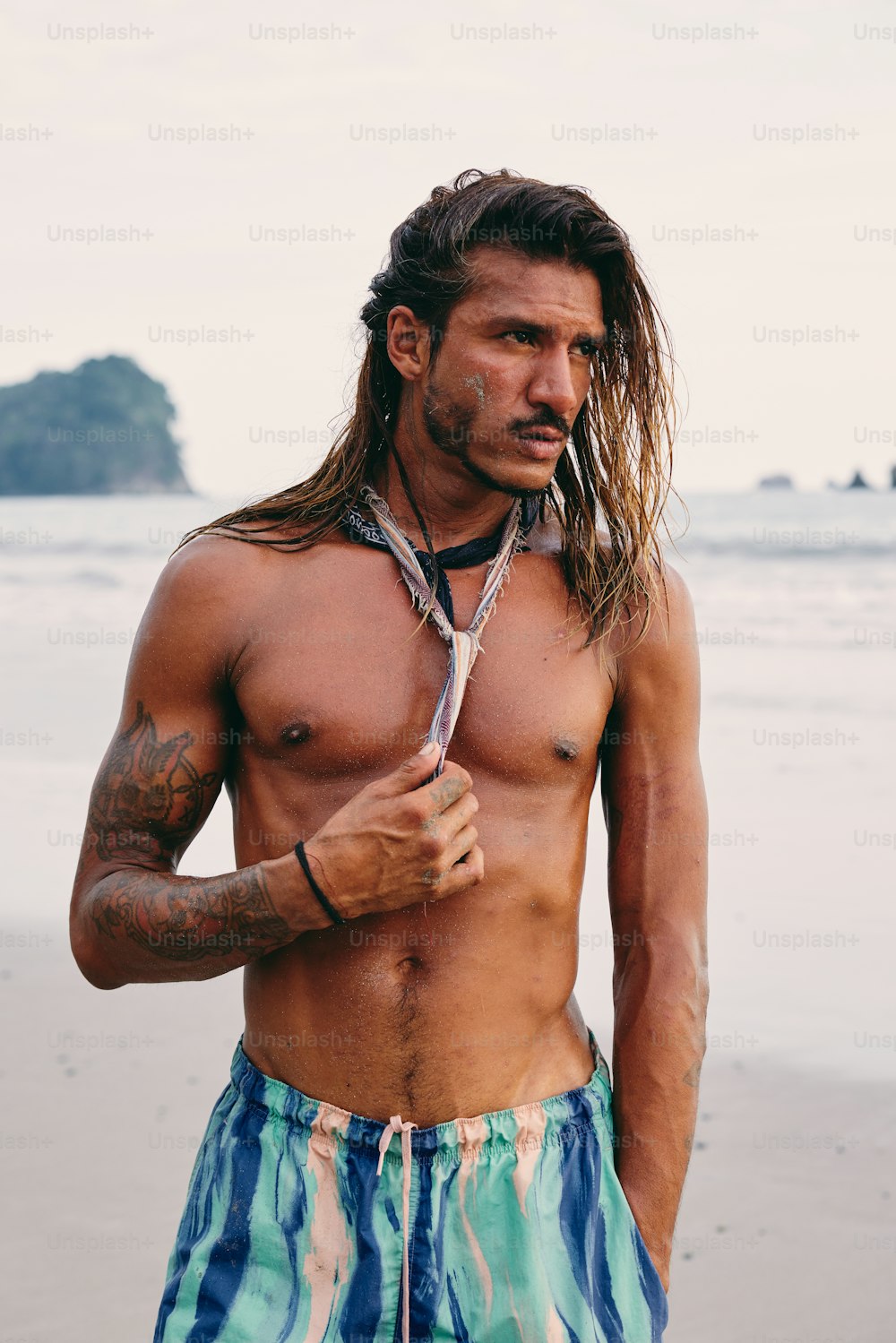 Un uomo a torso nudo in piedi su una spiaggia con un paio di forbici