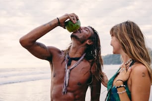 a man drinking a beer next to a woman on the beach