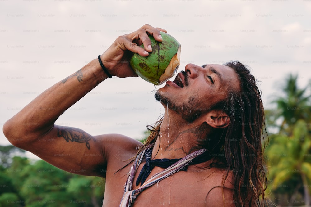 a man with long hair drinking from a coconut