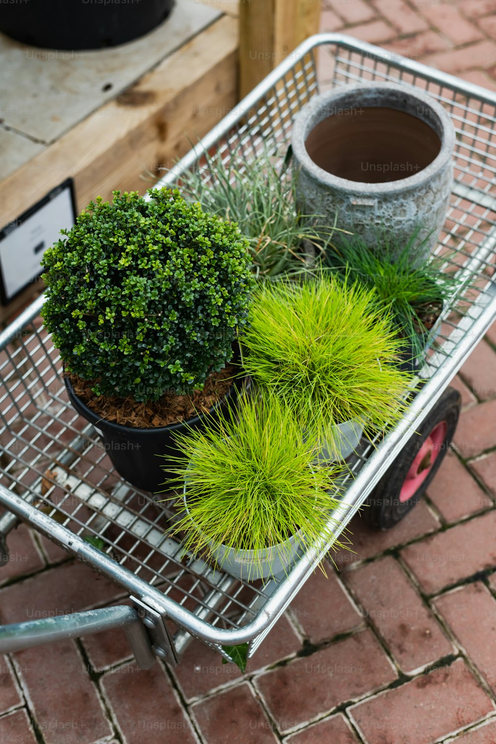 a shopping cart filled with potted plants on top of a brick floor
