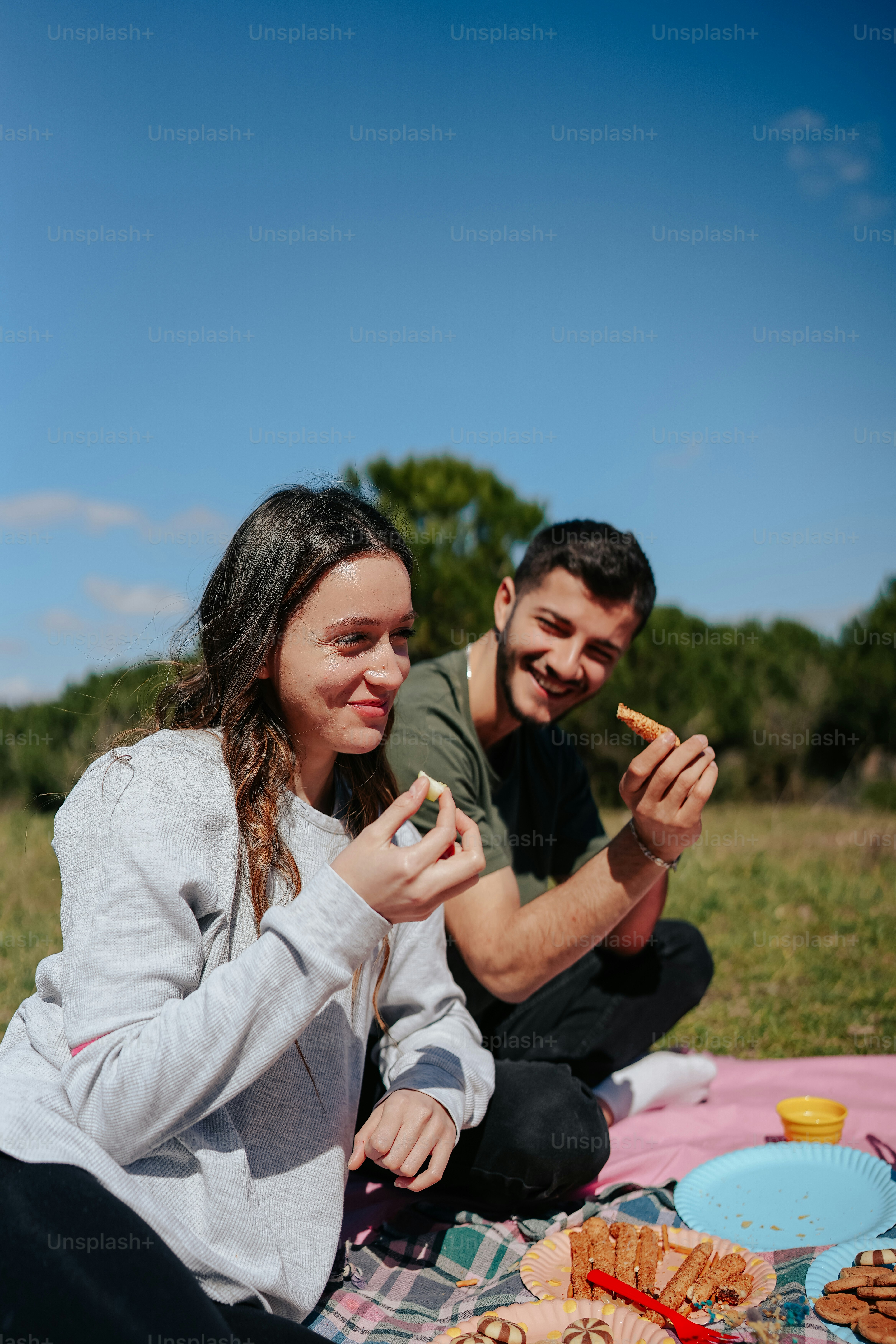 a man and a woman sitting on a blanket eating food