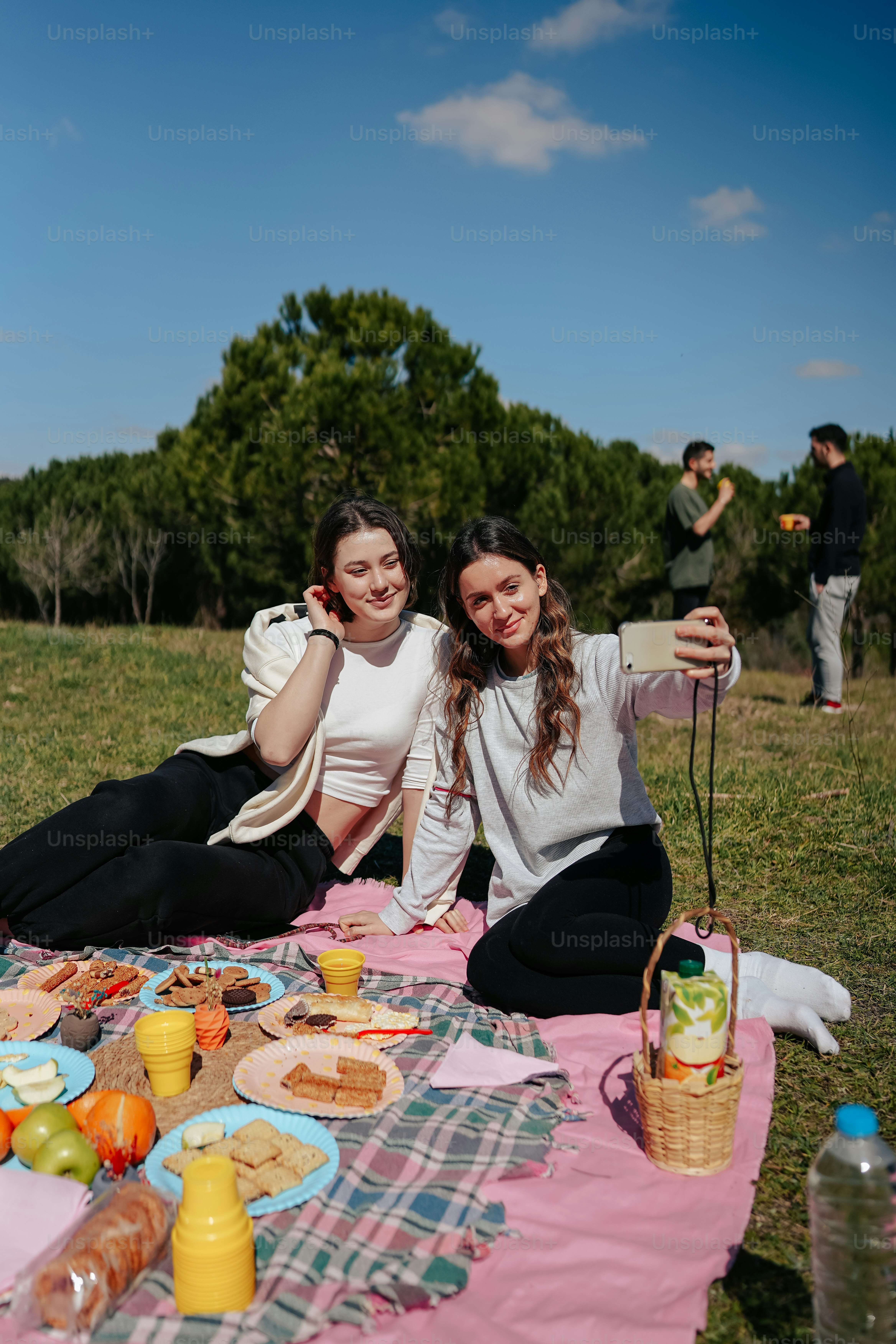 two women sitting on a blanket with food on the ground