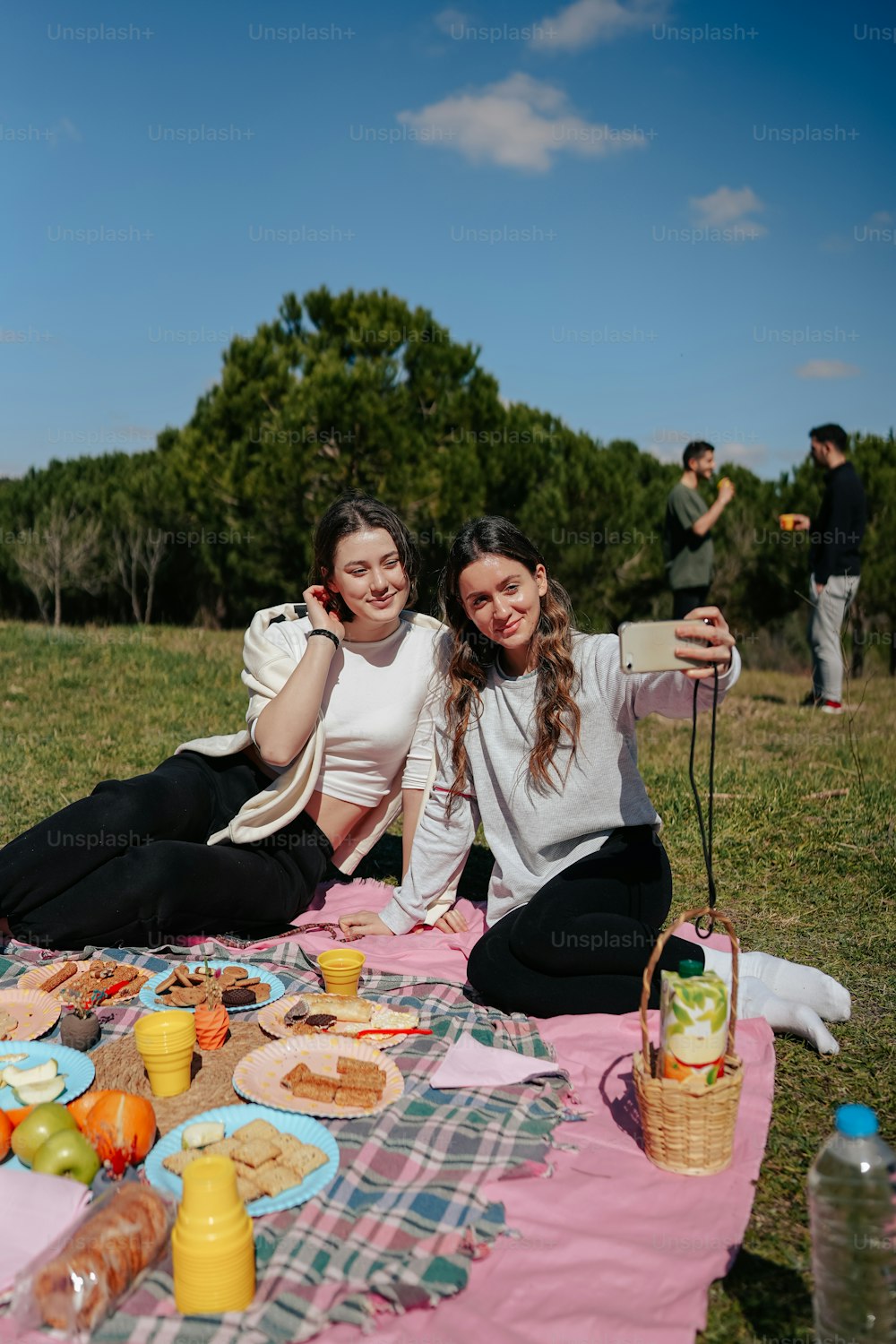 two women sitting on a blanket with food on the ground