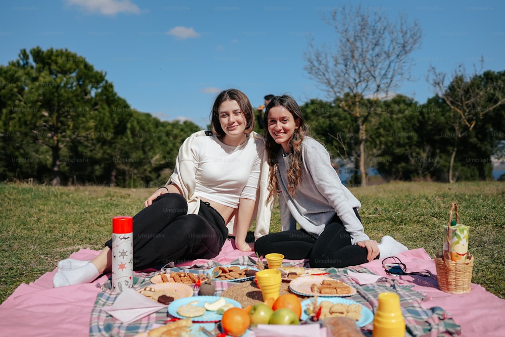 two women sitting on a blanket in the grass