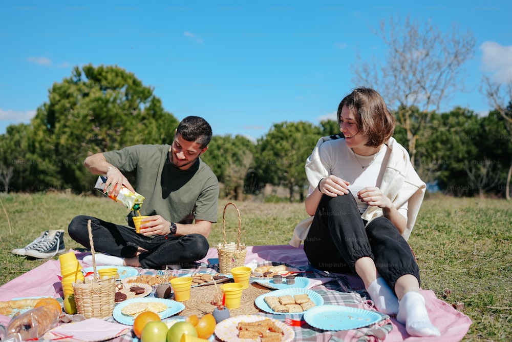 a man and a woman sitting on a blanket eating food