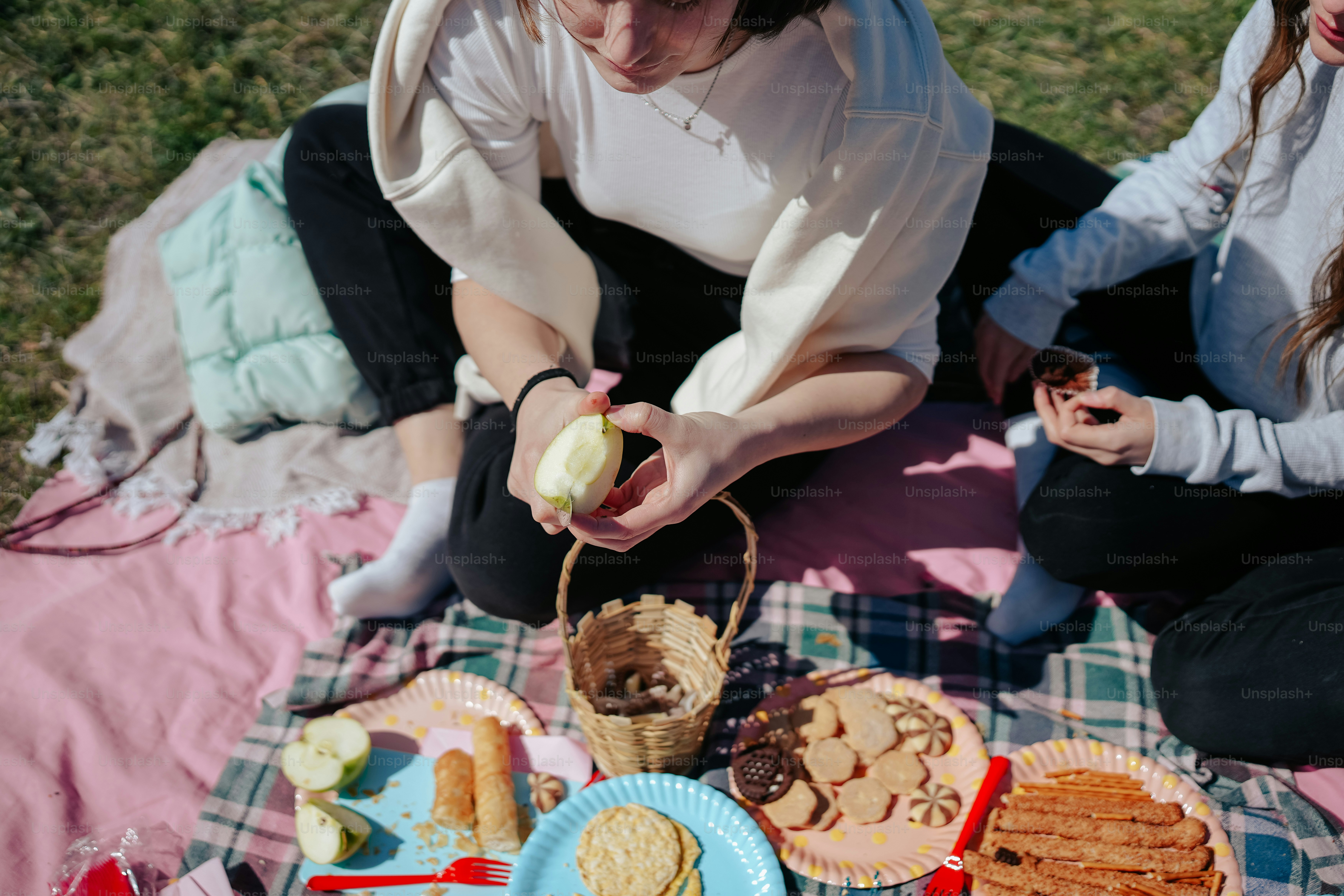 two women sitting on a blanket eating food