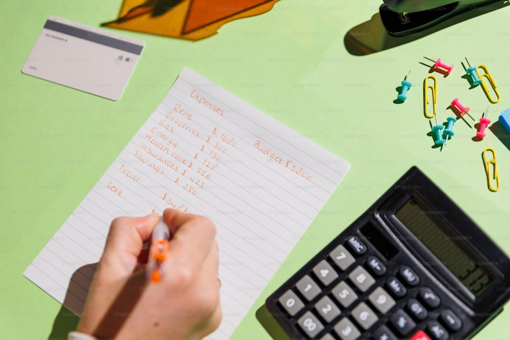 uma pessoa escrevendo em um pedaço de papel ao lado de uma calculadora