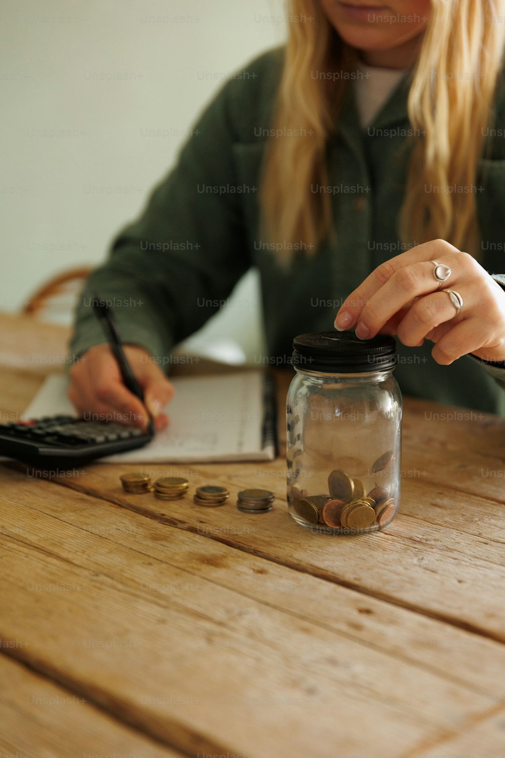 a woman sitting at a table with a jar of coins and a calculator