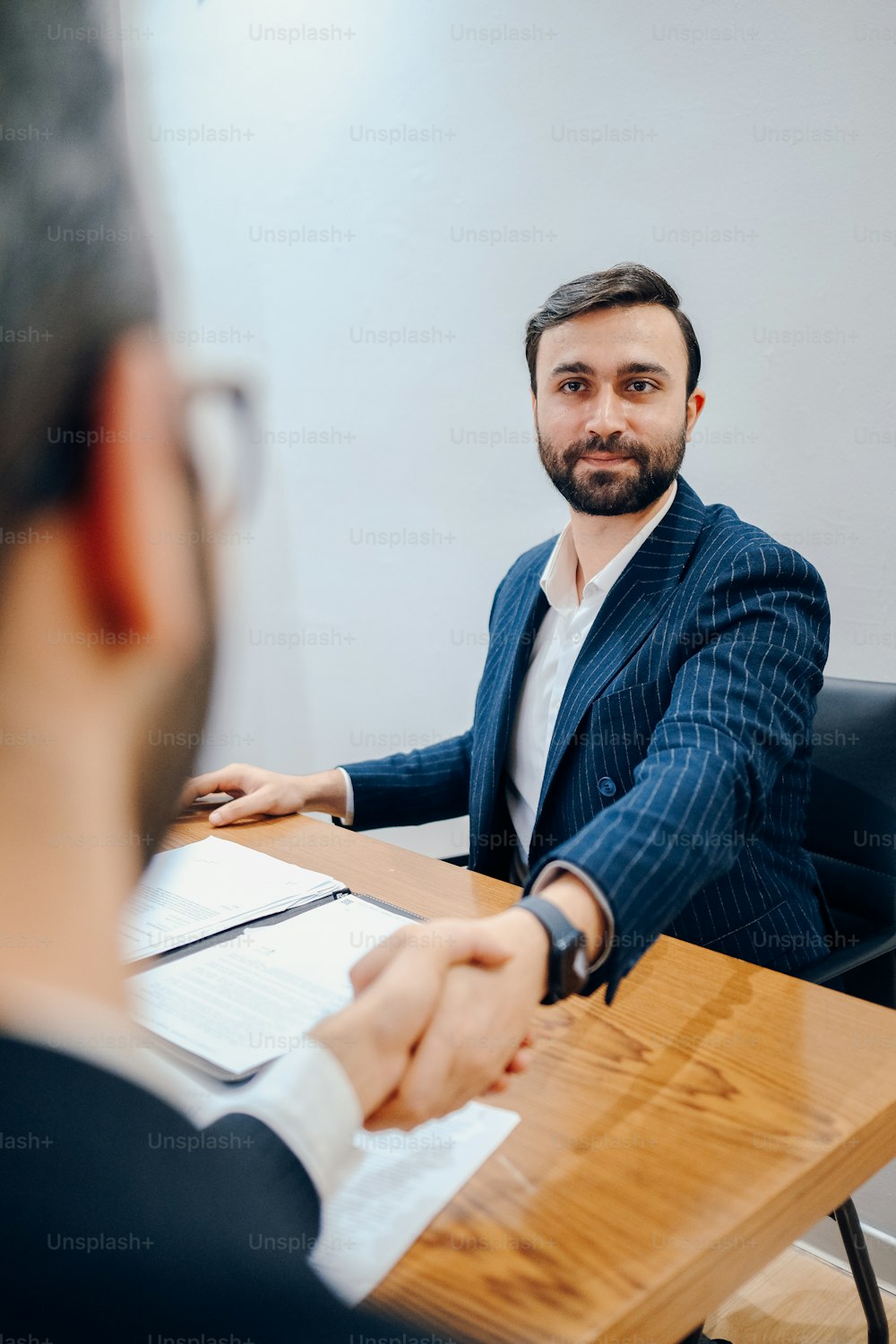 a man sitting at a desk shaking hands with another man