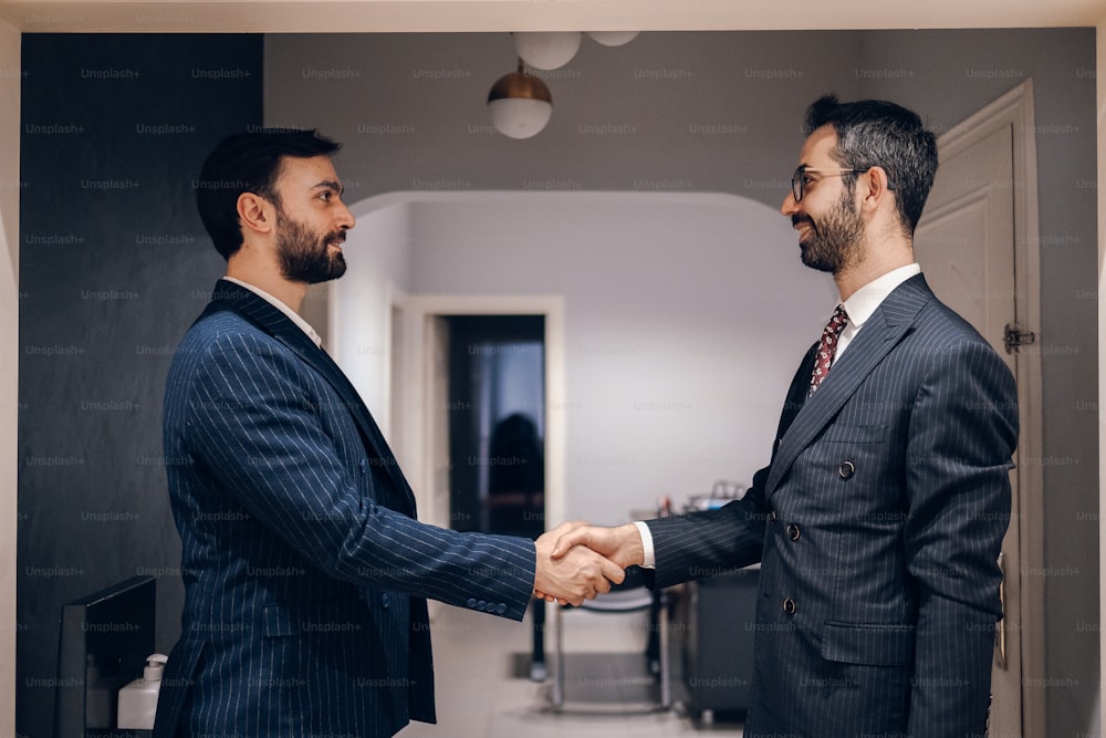 two men in suits shaking hands in a hallway