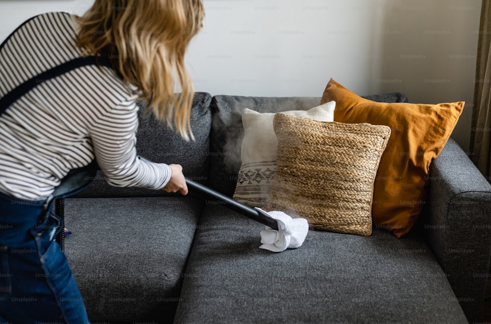 a woman cleaning a couch with a vacuum