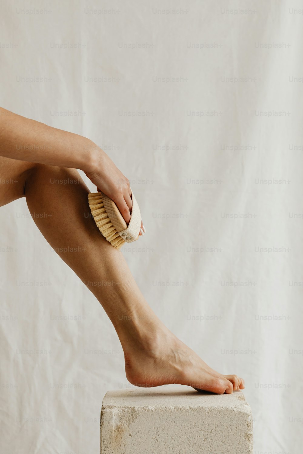 Las piernas desnudas de una mujer con un cepillo encima de un bloque de concreto