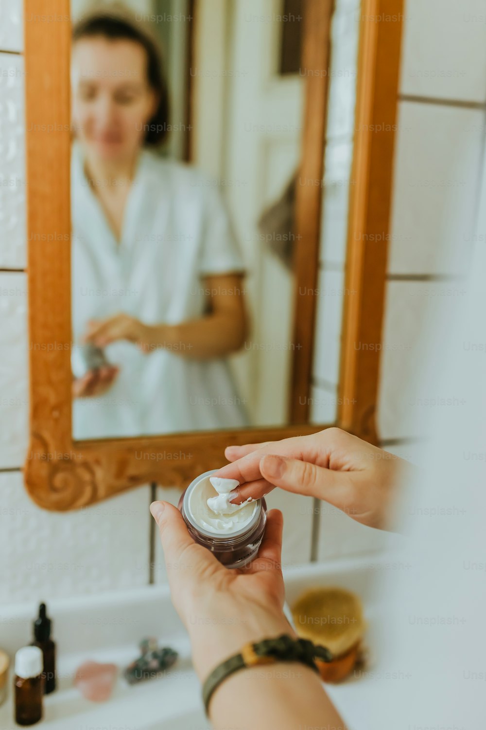 Una mujer sostiene un frasco de crema frente a un espejo