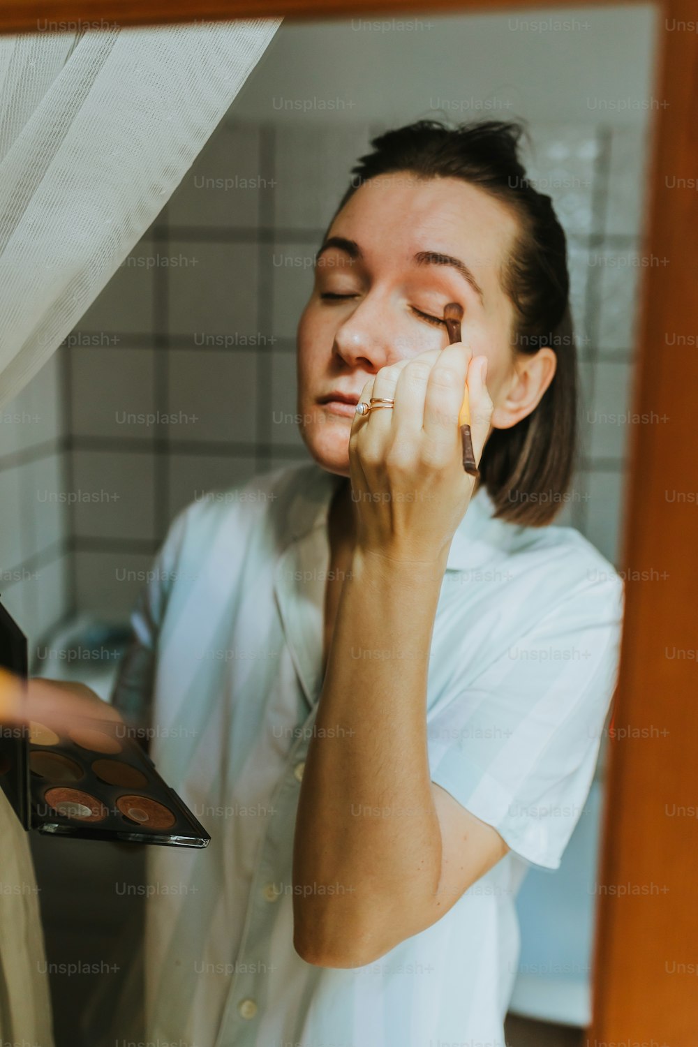 a woman putting makeup on her face in front of a mirror
