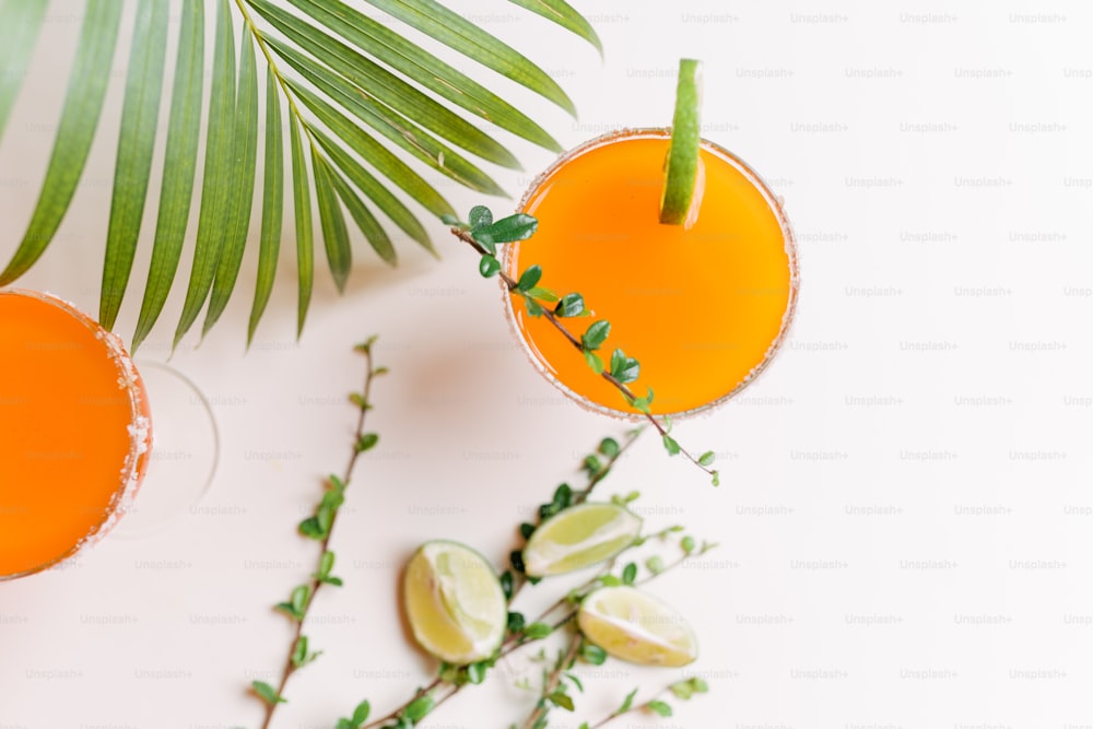 two glasses of orange juice next to a palm leaf