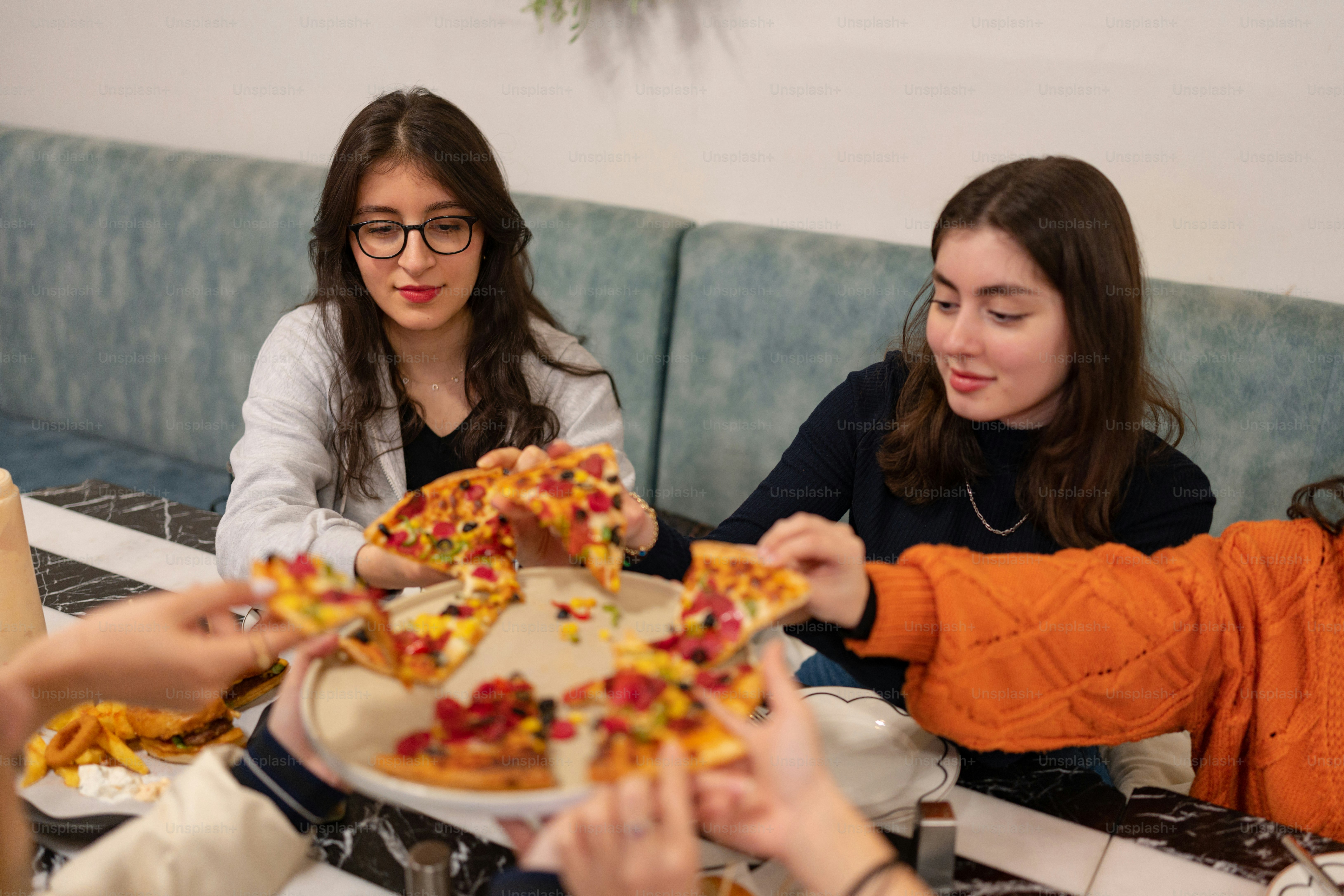 a group of women sitting around a table eating pizza