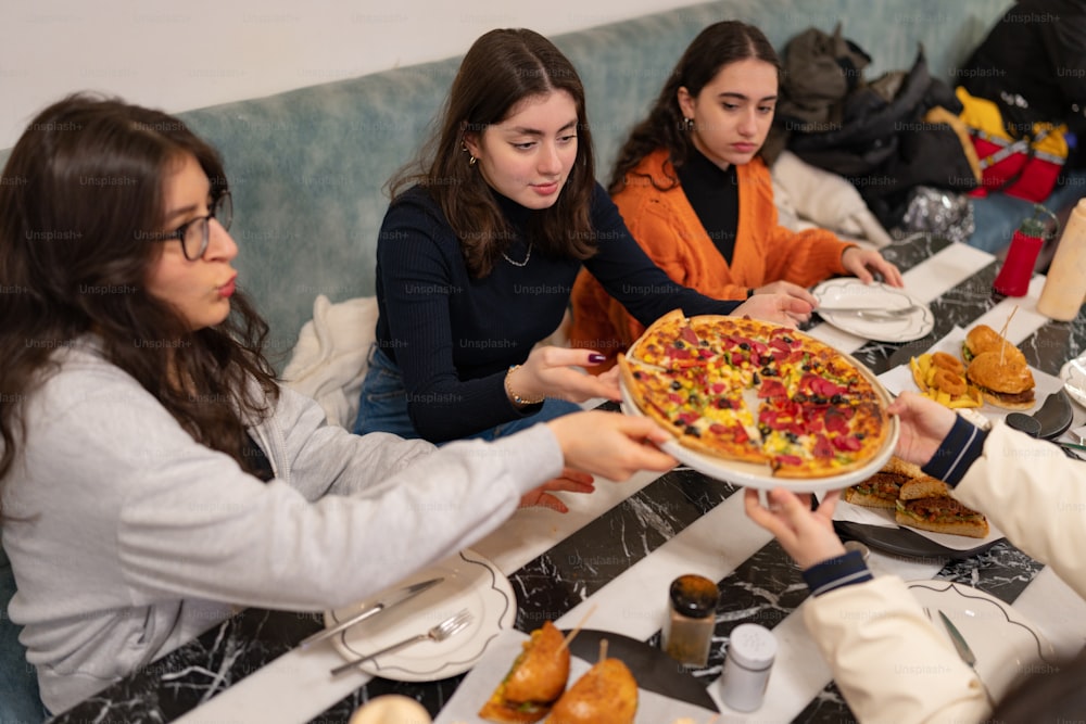 a group of women sitting at a table with a pizza