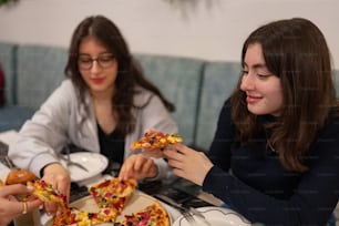 two women sitting at a table eating pizza