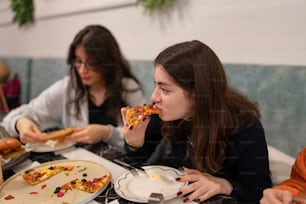 two women sitting at a table eating pizza