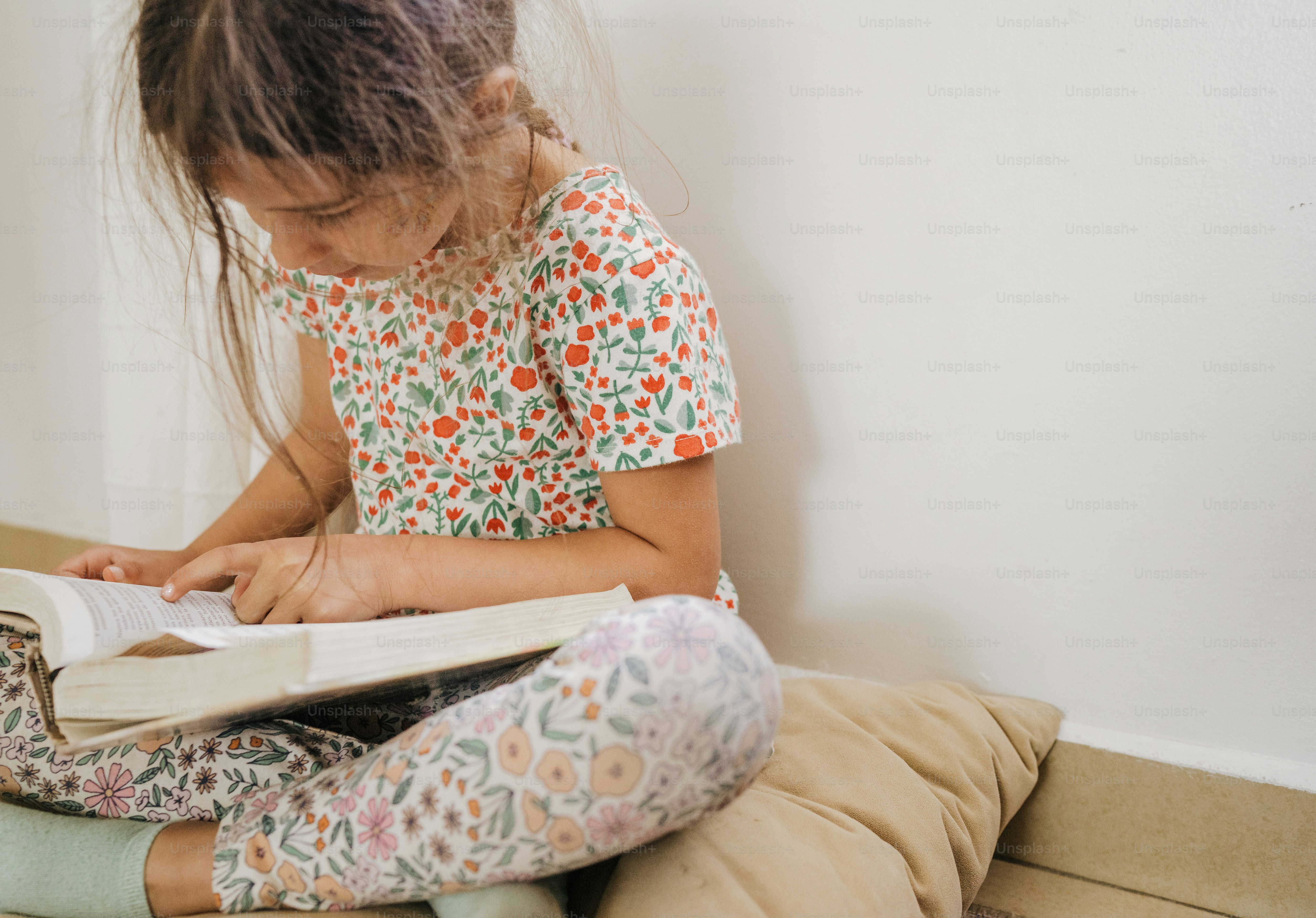 a little girl sitting on the floor reading a book