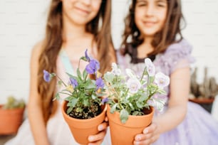 Dos niñas sosteniendo plantas en macetas en sus manos