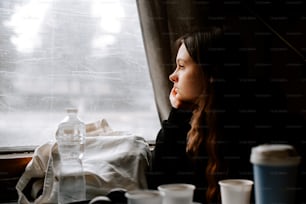 a woman looking out of a window with cups on a table