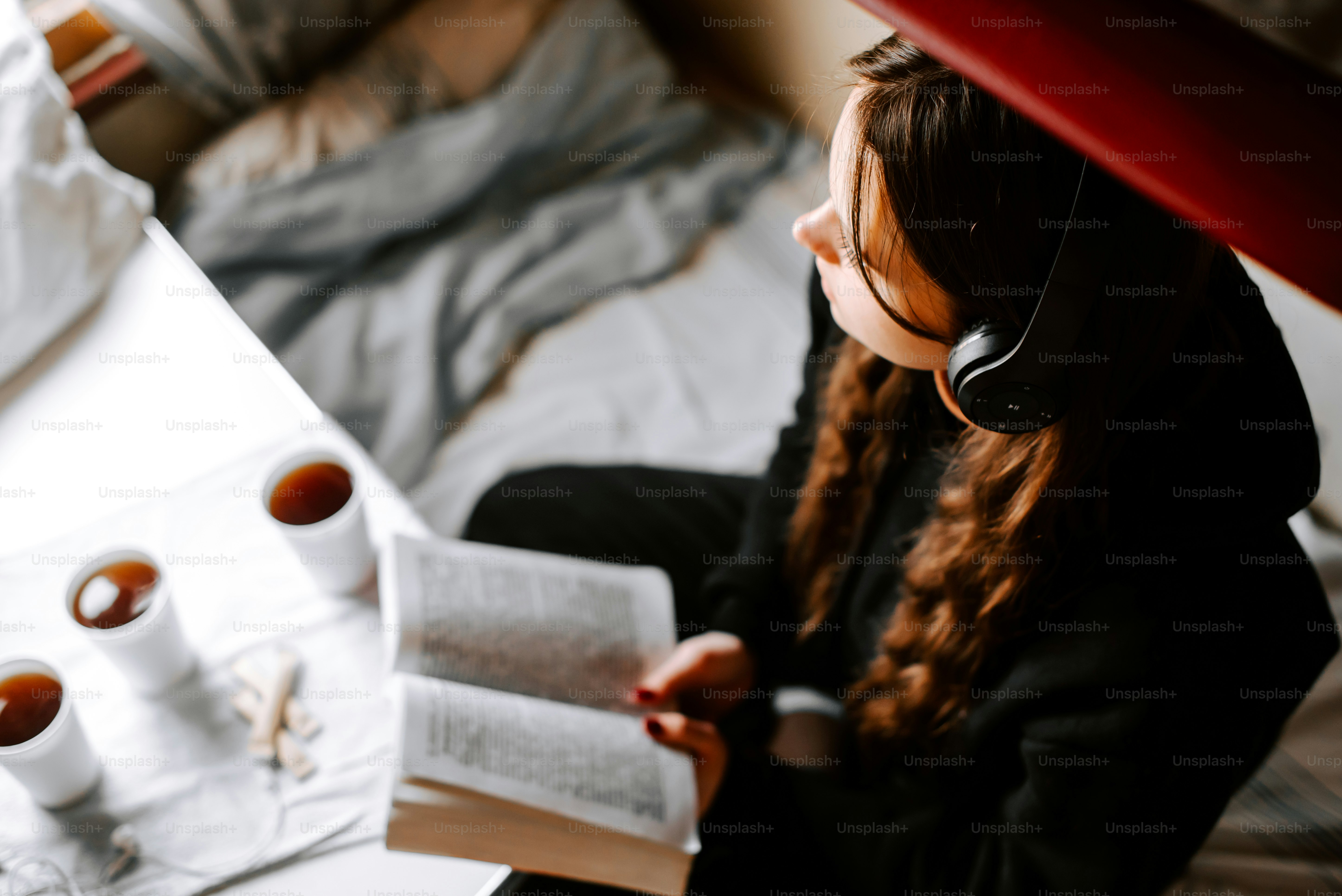 a woman sitting on a bed reading a book and listening to headphones
