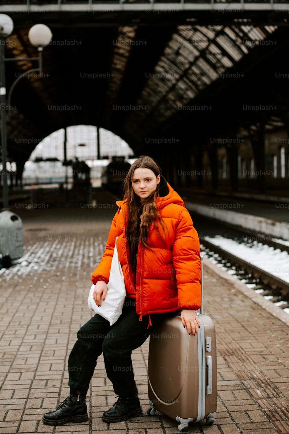 uma mulher em uma jaqueta laranja está sentada em uma mala